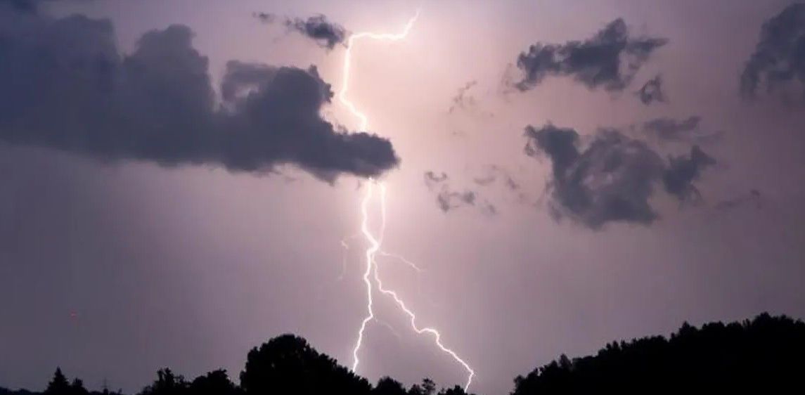 Ein Blitz schlägt mit Bäumen im Vordergrund unter dunklen, stürmischen Wolken in den Himmel ein.