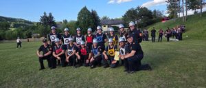 Eine Gruppe von Feuerwehrleuten in Uniformen und Helmen posiert für ein Foto auf einem Feld, mit mehreren anderen im Hintergrund.