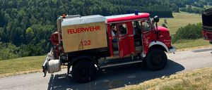A red fire truck with the number 122 is driving on a mountain road with lush green trees in the background.