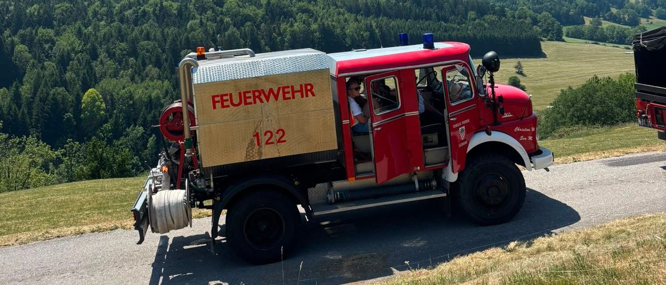 Ein roter Feuerwehrwagen mit der Nummer 122 fährt auf einer Bergstraße mit üppigem grünen Bäumen im Hintergrund.