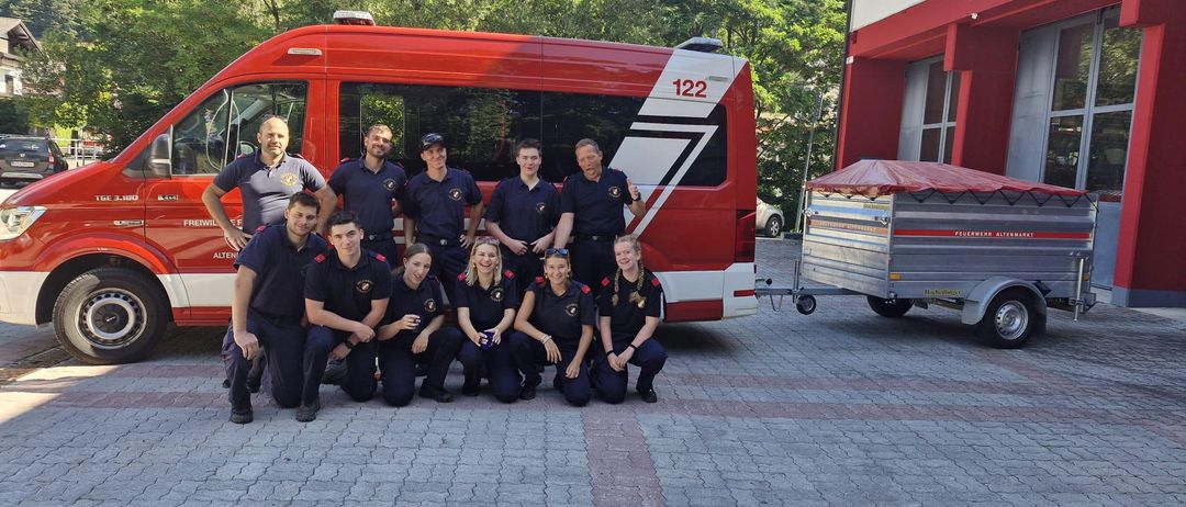 Eine Feuerwehrmannschaft posiert für ein Foto vor einem roten Feuerwehrwagen. Das Team trägt ihre Uniformen. Der Wagen hat die Nummer 122.