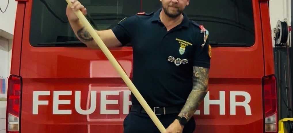Ein Feuerwehrmann in Uniform hält eine große Paddel vor einem roten Feuerwehrwagen mit der Aufschrift Altenmarkt.