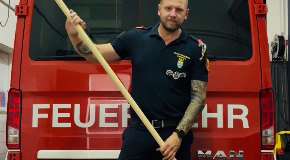 Ein Feuerwehrmann in Uniform hält eine große Paddel vor einem roten Feuerwehrwagen mit der Aufschrift Altenmarkt.