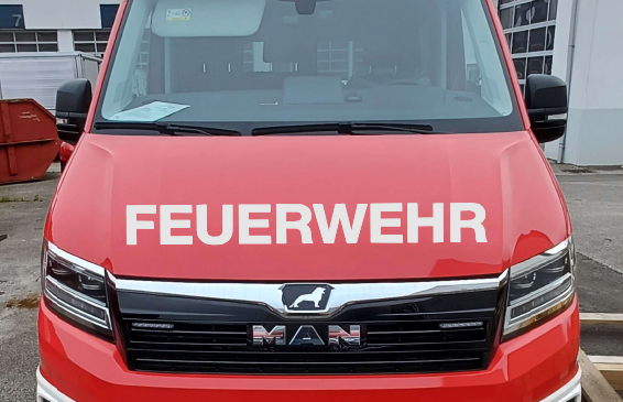Ein roter MAN-Lkw mit den Aufschriften 'Altenmarkt' und 'Feuerwehr' steht vor einem Gebäude. Der vordere Stoßfänger hat ein weißes Design und ein schwarzes Nummernschild. Eine Nummer 13 befindet sich an der Seite des Gebäudes.