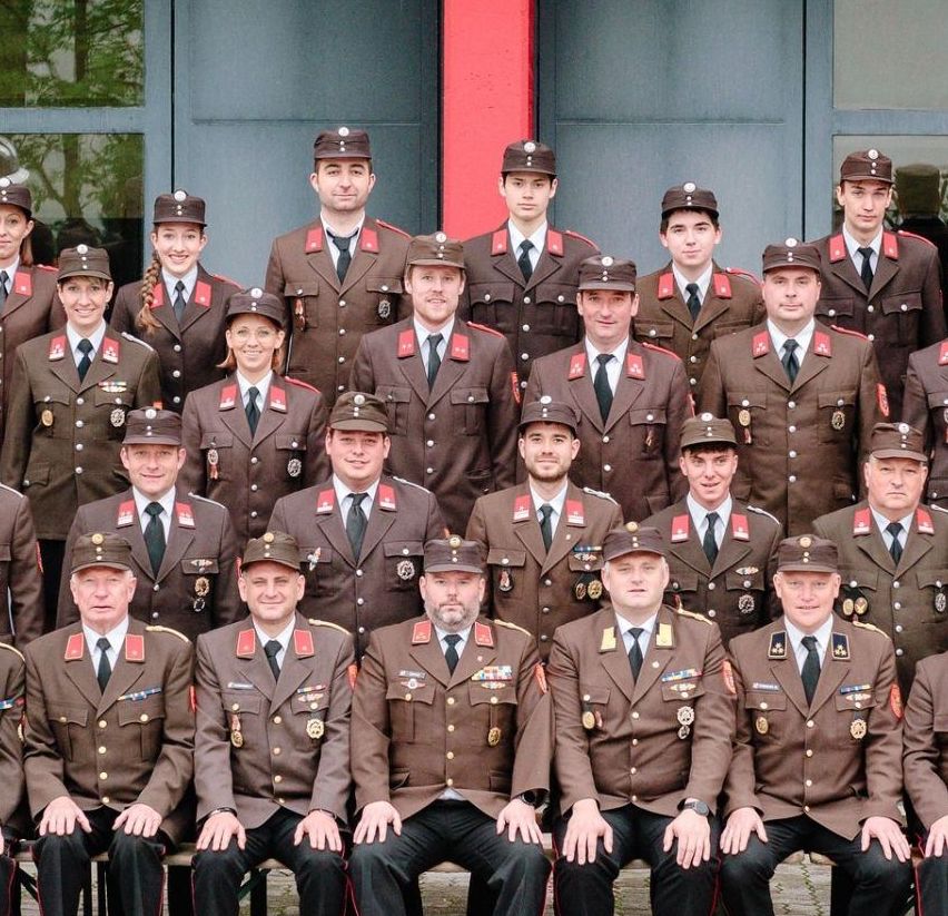 Eine Gruppe uniformierter Personen, wahrscheinlich eine Militär- oder Polizeieinheit, posiert für ein Foto vor einem modernen Gebäude mit Glaswänden.