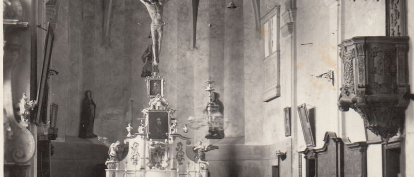 Ein altes Schwarz-Weiß-Foto des Inneren einer Kirche, das ein Kreuz auf dem Altar und eine Statue von Jesus Christus zeigt.
