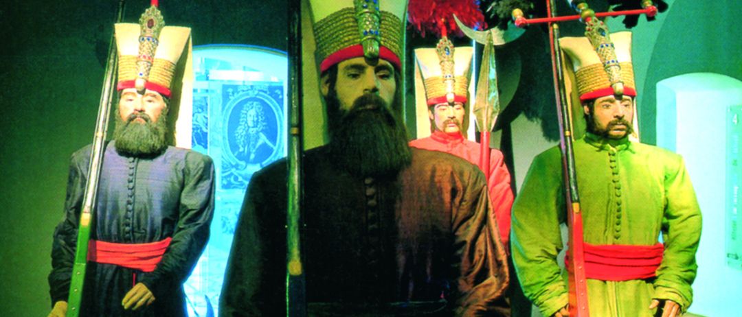 Vier Mannequins in altertümlicher Kriegerkleidung stehen in einem schwach beleuchteten Raum. Jeder hält eine Lanze und trägt aufwendige Kopfbedeckungen. Eines hält einen Schild mit einem Schiffsemblem.