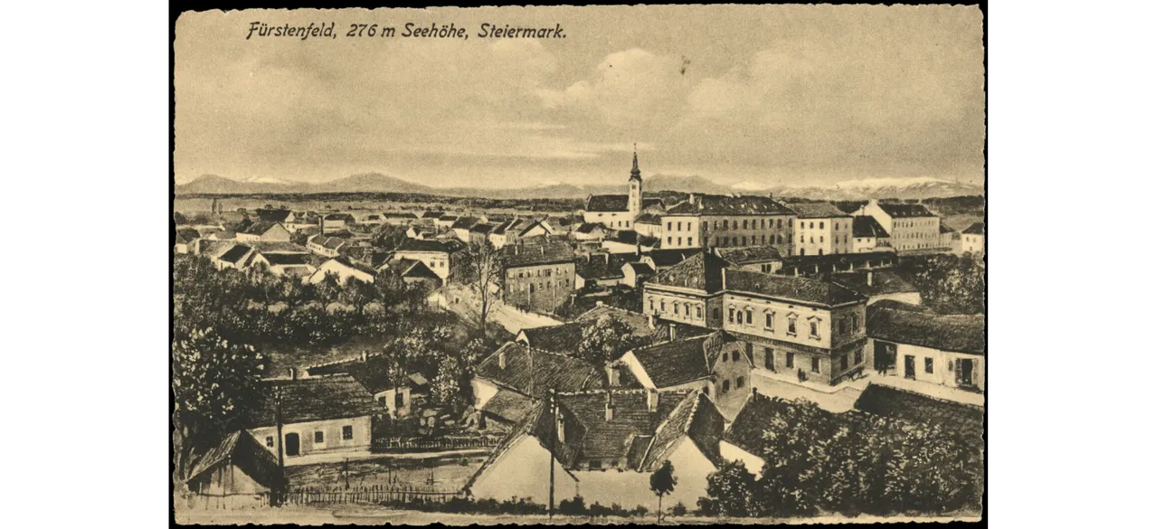 Ein altes Schwarz-Weiß-Foto von Furstenfeld, einer Stadt in der Steiermark, Österreich. Das Bild zeigt eine Panoramaansicht der Stadt mit mehreren Gebäuden, einem Turm und einer Kirche.