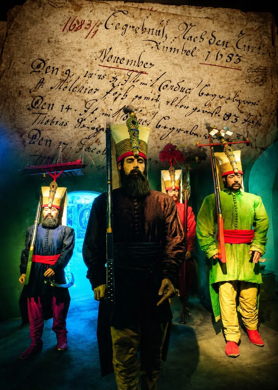 A group of men dressed in historical costumes stand in a dimly lit room. They are holding weapons and wearing ornate hats.