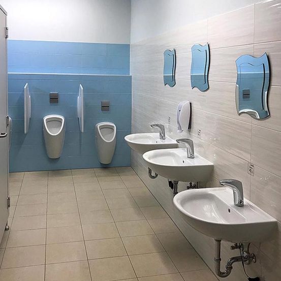 Eine saubere öffentliche Toilette mit drei Waschbecken und drei Urinalen. Es gibt Seifenspender und Spiegel an der Wand.