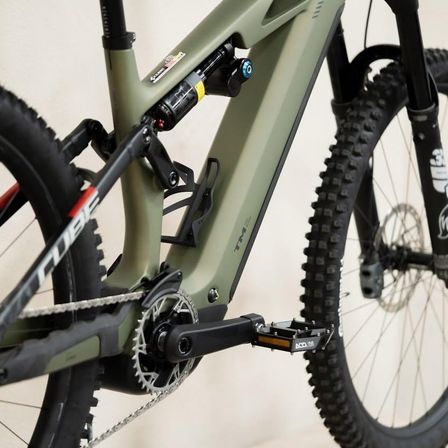 Nahaufnahme eines grünen Mountainbikes mit Stoßdämpfer hinten, Kette und Pedal. Das Fahrrad hat ein schwarzes und grünes Farbschema.