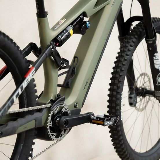 Nahaufnahme eines grünen Mountainbikes mit Stoßdämpfer hinten, Kette und Pedal. Das Fahrrad hat ein schwarzes und grünes Farbschema.