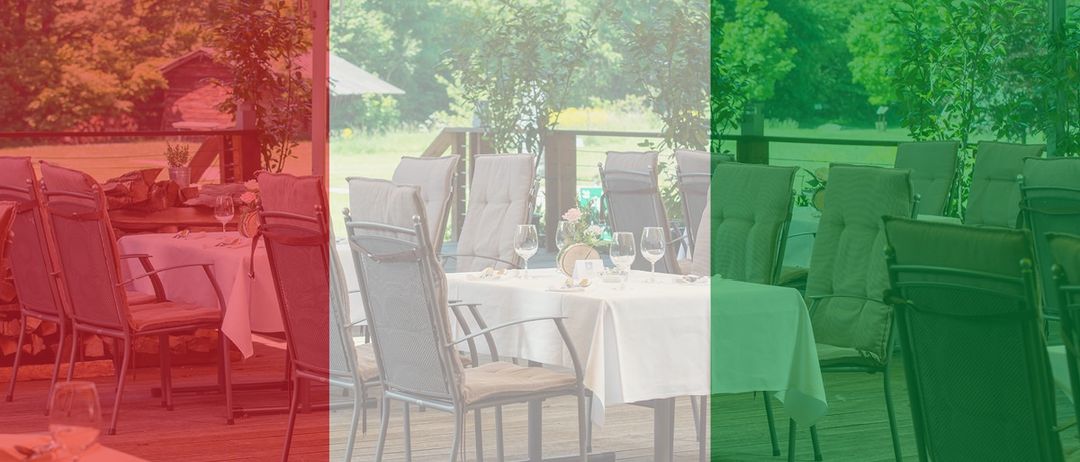 Ein Restaurant im Freien mit gedeckten Tischen, umgeben von üppigem Grün und einer entfernten Aussicht auf ein Feld.