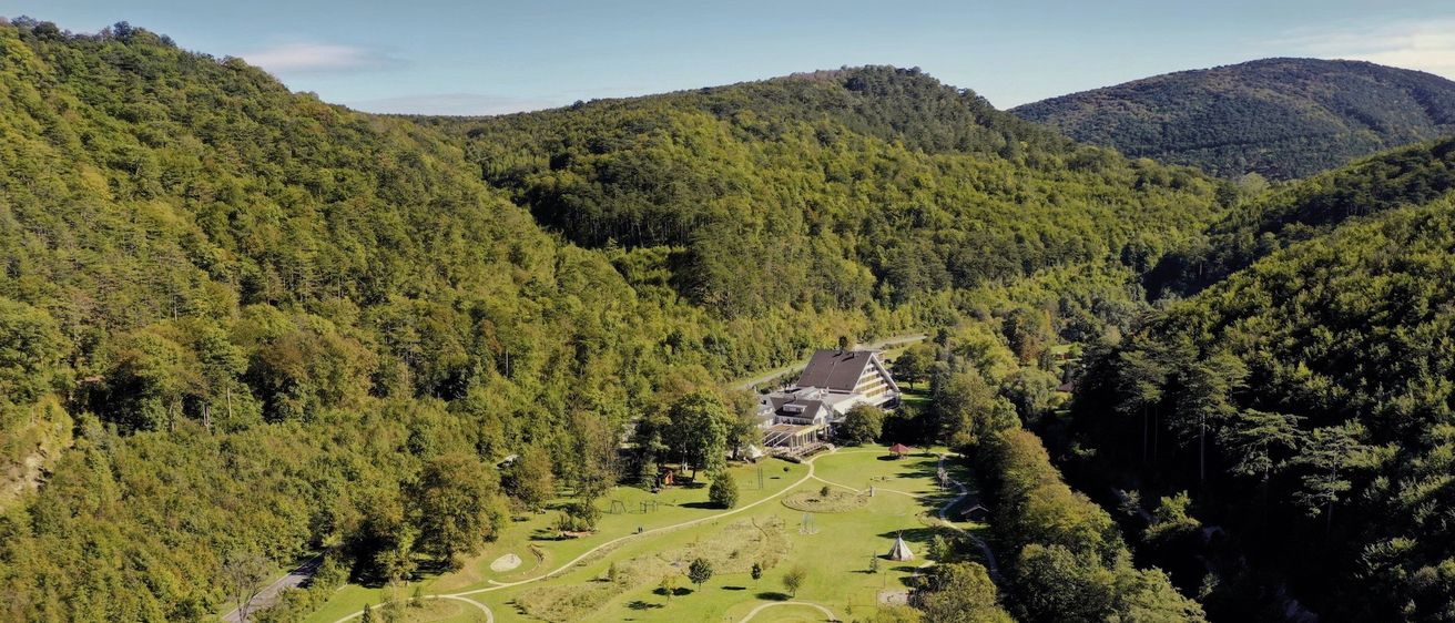 Ein Luftbild eines Golfplatzes inmitten eines üppigen Waldes, umgeben von dichten Bäumen und einem großen Gebäude in der Mitte.