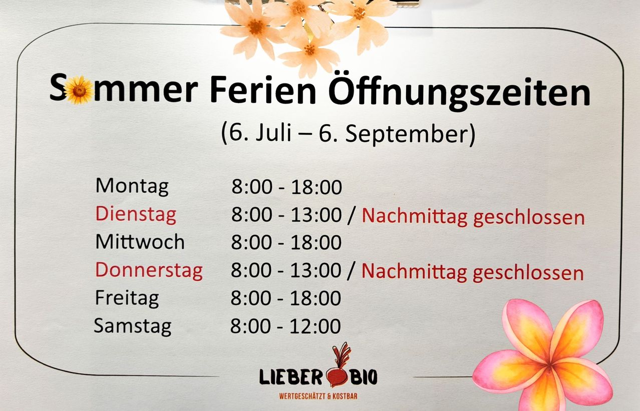 Ein Plakat listet die Öffnungszeiten der Sommerferien auf. Vom 6. Juli bis 6. September ist es von Montag bis Freitag von 8:00 bis 18:00 Uhr und samstags von 8:00 bis 13:00 Uhr nachmittags geöffnet.