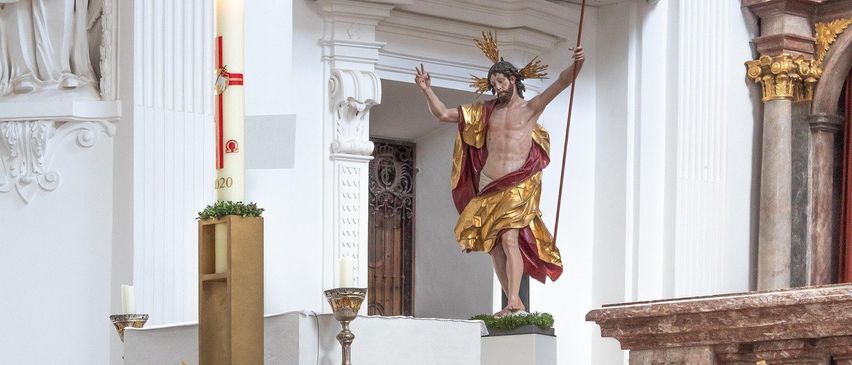 Eine goldene Statue von Jesus mit einem Stab mit einem Kreuz steht auf einer Plattform vor einer Kirche.