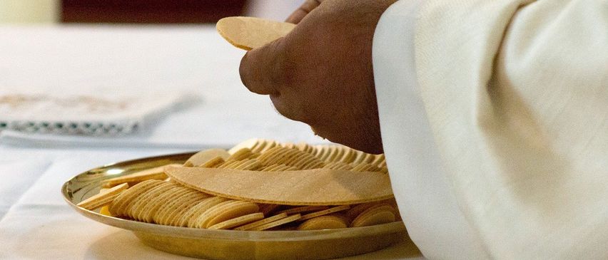 Eine Person in einer weißen Robe bereitet Oblaten für eine religiöse Zeremonie vor.
