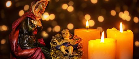 Eine Krippe mit Maria, die das Jesuskind hält, umgeben von brennenden Kerzen und Bokeh-Lichtern im Hintergrund.