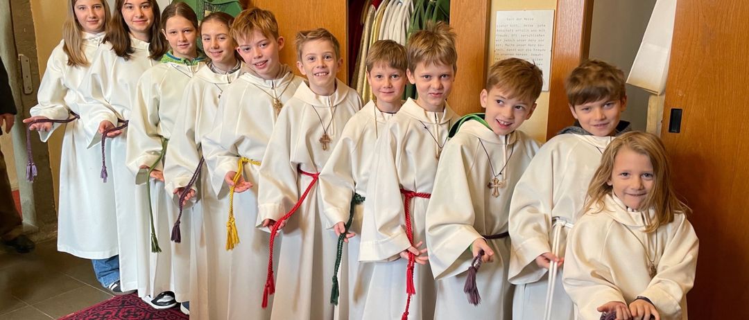 Eine Gruppe von Kindern in weißen Roben und roten Schärpen, die in einer Reihe stehen, möglicherweise für eine Schulveranstaltung.