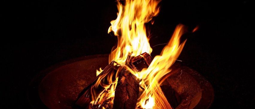 Ein Lagerfeuer brennt hell in einer Metallschüssel, mit Flammen, die nach oben springen und den dunklen Hintergrund erhellen.