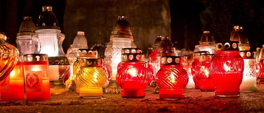 Eine Sammlung roter und gelber Glaslaternen mit Metalldeckeln ist in einem schwach beleuchteten Bereich beleuchtet, möglicherweise für eine Gedenkfeier oder religiöse Zeremonie.