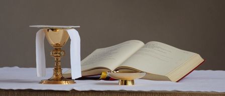 A golden chalice with a white cloth and an open book on a table.