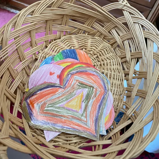 Ein Korb aus Weide gefüllt mit mehrfarbigen Herz-Papierausschnitten. Die Herzen sind in verschiedenen Farben und Mustern gestaltet.