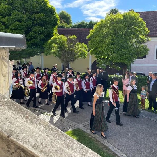 Eine Band in traditioneller Kleidung spielt Instrumente und marschiert in einer Parade vor einem Gebäude.