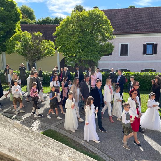 Eine Gruppe von Menschen, darunter Erwachsene und Kinder, gehen in einer Reihe vor einem Gebäude nach draußen. Einige halten Kerzen.