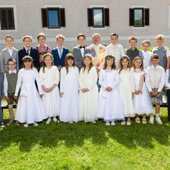 Eine Gruppe von Kindern und einigen Erwachsenen posiert für ein Foto vor einem Gebäude. Die Kinder sind in Weiß gekleidet und die Erwachsenen in formeller Kleidung.