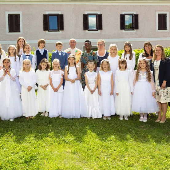 Eine Gruppe von Kindern und Erwachsenen, in Weiß gekleidet, posiert für ein Foto vor einem Gebäude.