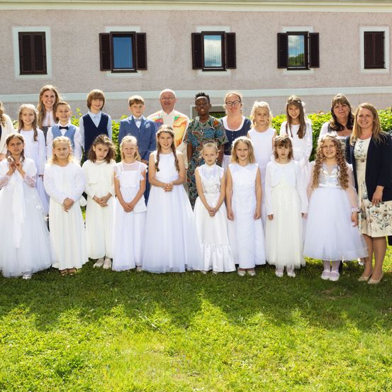 Eine Gruppe von Kindern und Erwachsenen, in Weiß gekleidet, posiert für ein Foto vor einem Gebäude.