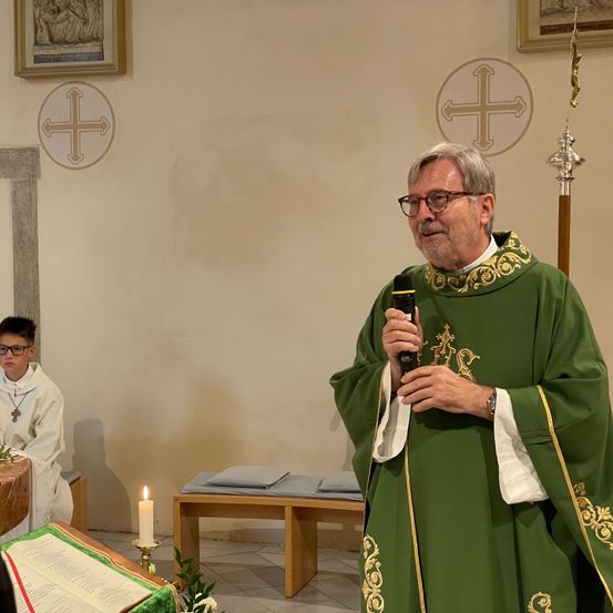 Ein Priester hält in einer Kirche eine Rede, hält ein Mikrofon in der Hand, mit einem jungen Jungen in einer weißen Robe in der Nähe.