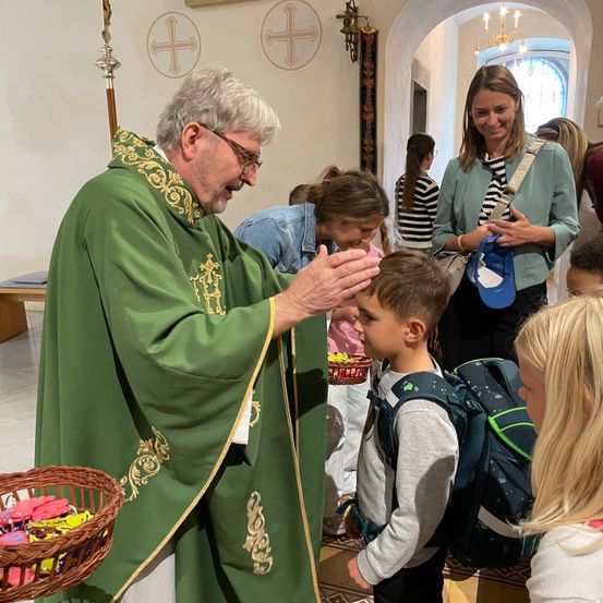 Ein Priester in einem grünen Gewand segnet einen jungen Jungen, während andere in einer Kirche zusehen.