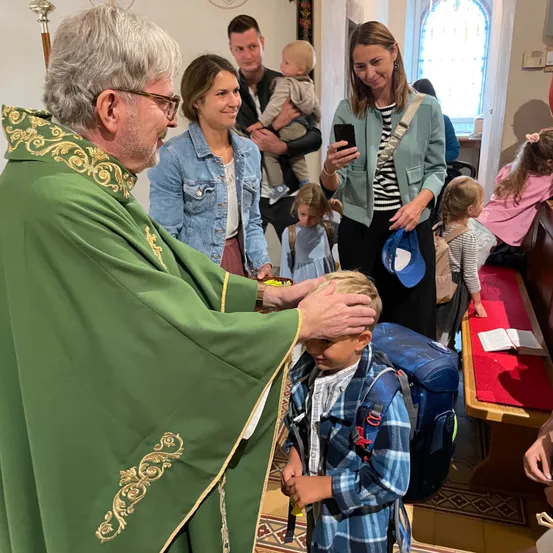 Ein Priester segnet einen kleinen Jungen während eines Gottesdienstes. Eltern und Kinder sind anwesend, und eine Frau hält ein Baby.