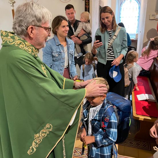 Ein Priester segnet einen kleinen Jungen während eines Gottesdienstes. Eltern und Kinder sind anwesend, und eine Frau hält ein Baby.