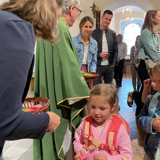 Ein Priester gibt einem Kind in einer Kirche einen Korb mit Ostereiern. Eine Frau und ein Mann stehen neben dem Kind.