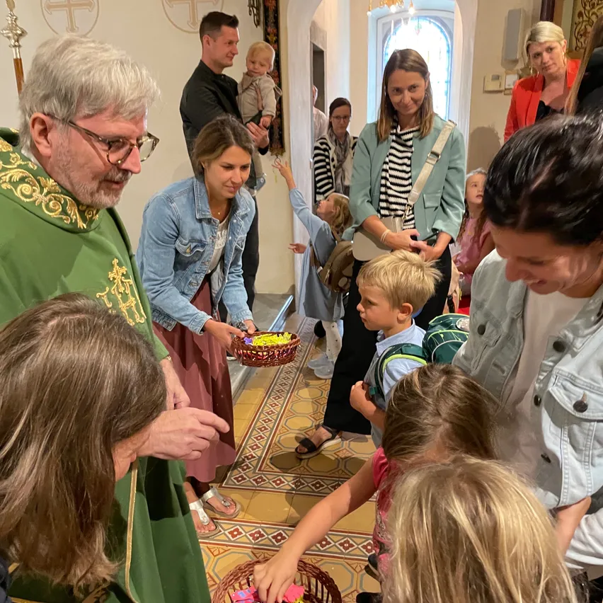 Ein Priester in einer grünen Robe verteilt Ostereier an Kinder in einer Kirche, während Erwachsene zusehen.