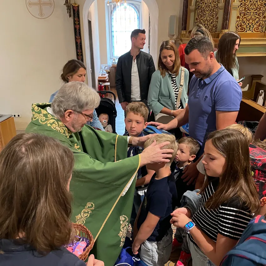 Ein Priester in einer grünen Robe segnet einen jungen Jungen in einer Kirche, während andere Familien zuschauen.