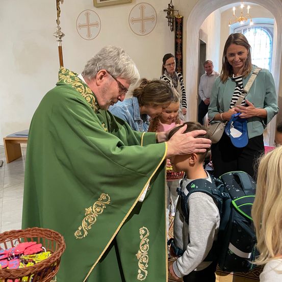 Ein Priester in einem grünen Gewand segnet einen Jungen, umgeben von anderen Menschen, in einer Kirche.