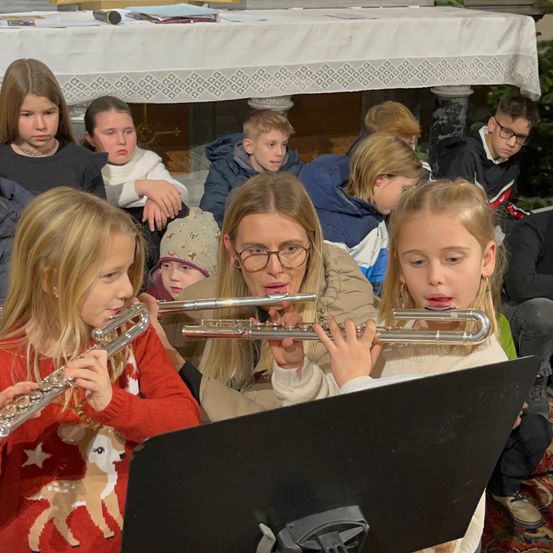 Eine Gruppe von Kindern und Erwachsenen sitzt in einer Kirche. Einige Kinder spielen Flöten. Andere sitzen und beobachten sie.