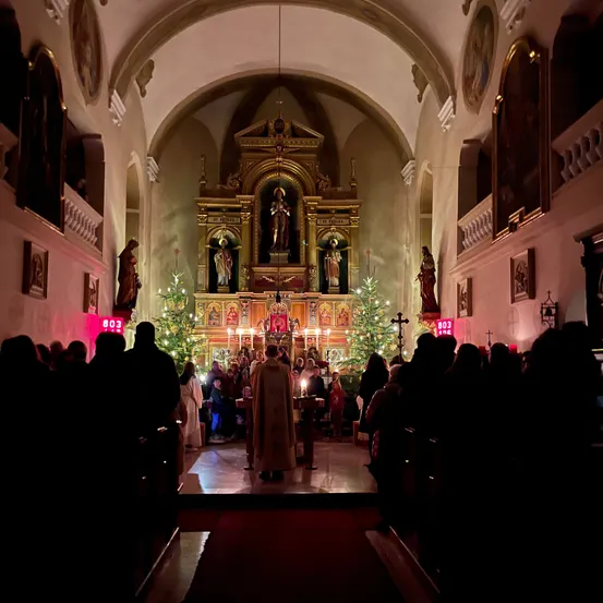 Eine Gruppe von Menschen besucht einen Weihnachtsgottesdienst in einer Kirche, beleuchtet von Kerzen und geschmückt mit Weihnachtsbäumen.