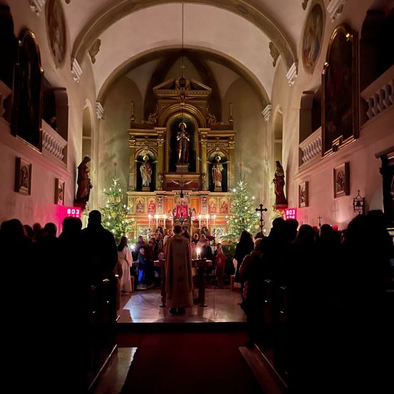 Eine Gruppe von Menschen besucht einen Weihnachtsgottesdienst in einer Kirche, beleuchtet von Kerzen und geschmückt mit Weihnachtsbäumen.