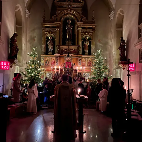 Eine weihnachtliche Zeremonie in einer Kirche mit Weihnachtsbäumen, Musikern und Teilnehmern vor einem Altar.