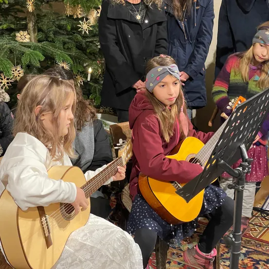 Eine Gruppe junger Mädchen spielt Gitarren in einem Raum, möglicherweise für eine Aufführung. Der Raum ist für Weihnachten geschmückt.