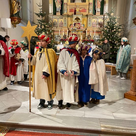 Eine Gruppe von Kindern in traditionellen Kostümen steht während einer Weihnachtszeremonie in einer Kirche, hält einen Stern und steht vor einem geschmückten Altar.