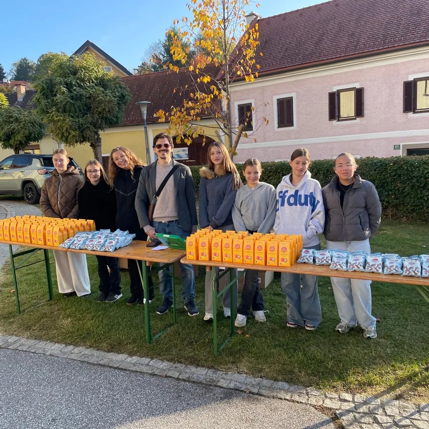 Eine Gruppe von Menschen steht vor einem Tisch mit Essensartikeln darauf. Sie alle lächeln und scheinen für ein Foto zu posieren.