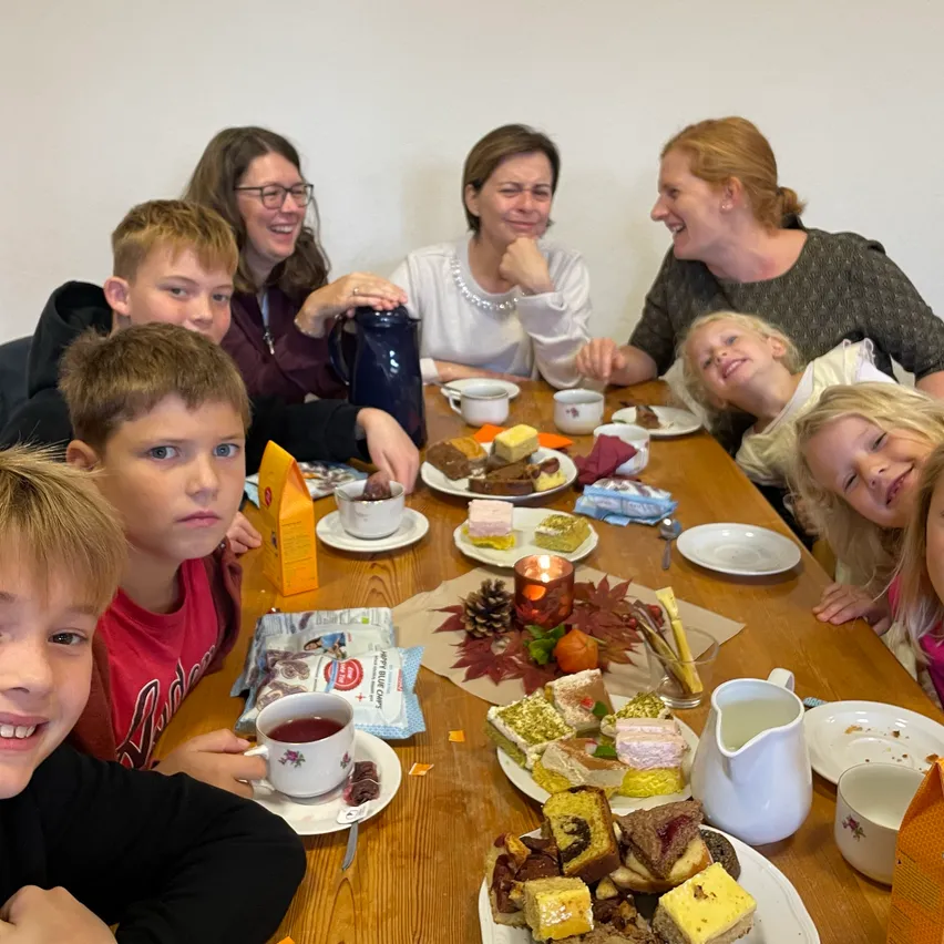 Eine Gruppe von Menschen, einschließlich Erwachsener und Kinder, sitzt um einen Tisch mit Essen und Getränken.