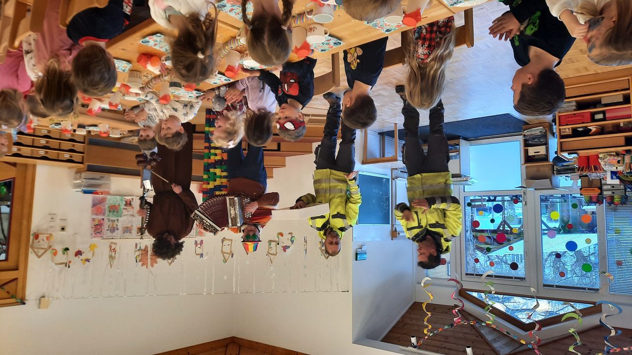 Eine Gruppe von Kindern und Erwachsenen steht in einem festlichen Raum auf dem Kopf, einige spielen Instrumente und andere posieren für ein Foto.