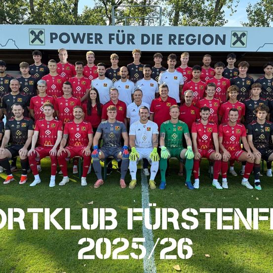 Eine Fußballmannschaft posiert für ein Foto auf einem Feld, in roten und weißen Trikots gekleidet. Ein Banner hinter ihnen trägt den Text 'Power für die Region'. Die Mannschaft ist als 'Sportklub Furstenfeld 2025/26' beschriftet.